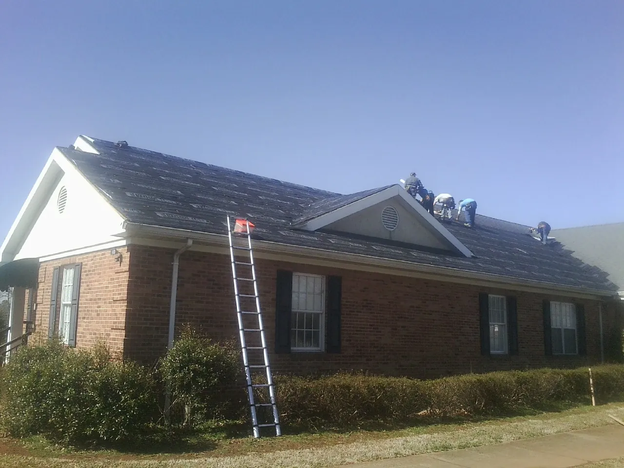 Crew tearing shingles off a brick ranch roof with a ladder set — Metal Roof Repair work by our crew in Sandusky