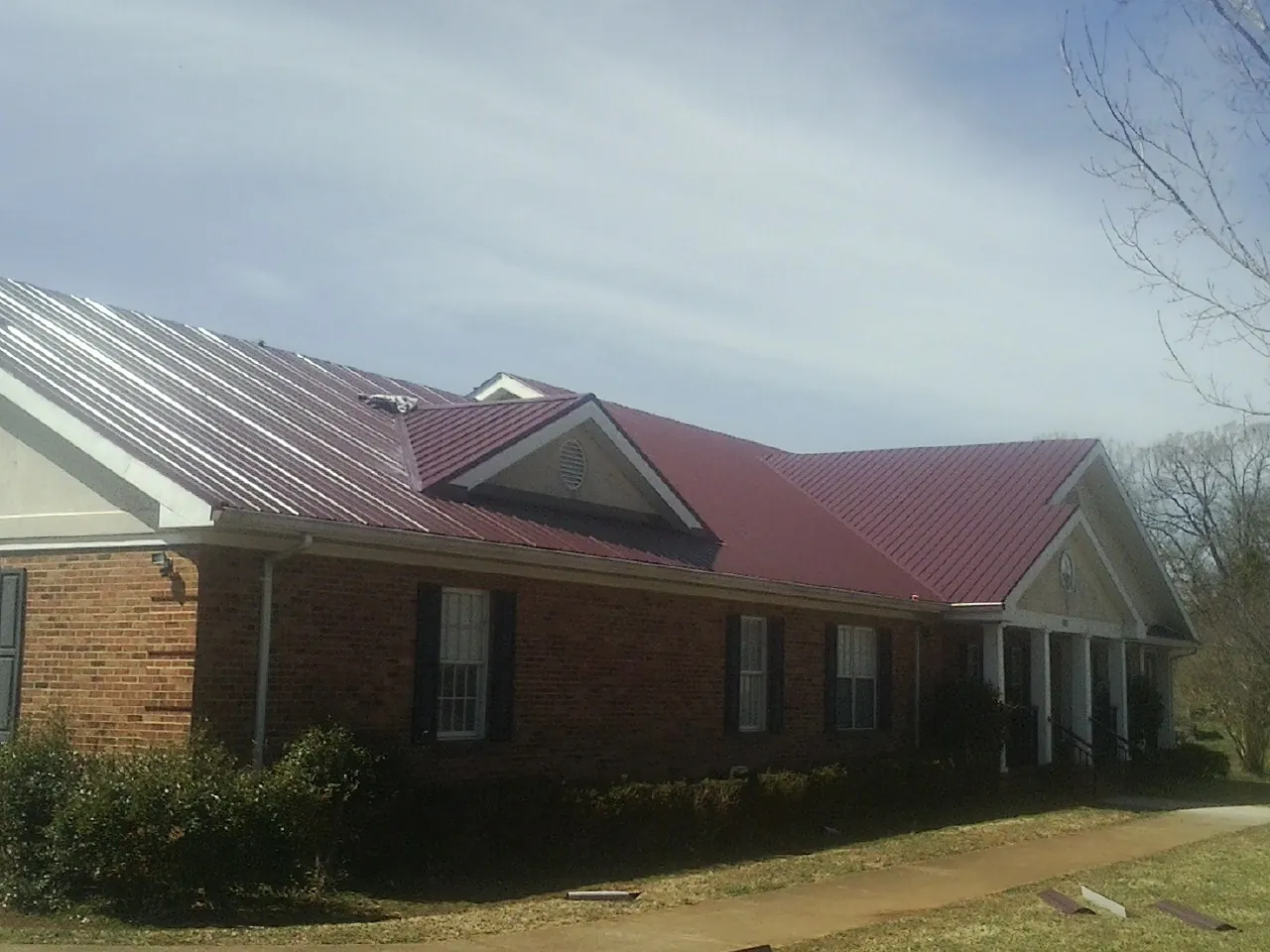 Red metal roof with gabled entries on a long brick building, from a Hail Damage Roof Repair job in Sandusky