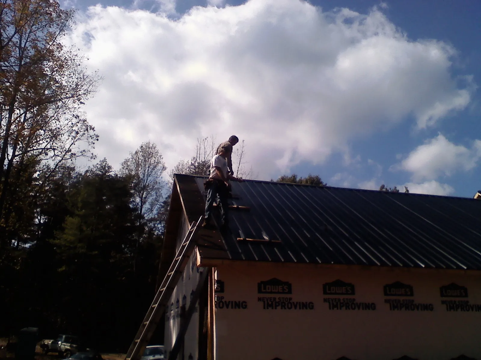 Roofer fastening dark metal panels high against a cloudy sky, from a Roof Inspection job in Sandusky